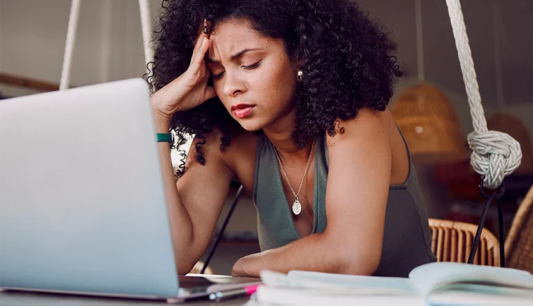 uma mulher em frente ao computador, de olhos fechados e com uma mão pousada na testa, demonstrando frustração porque sente a sua carreira estagnada