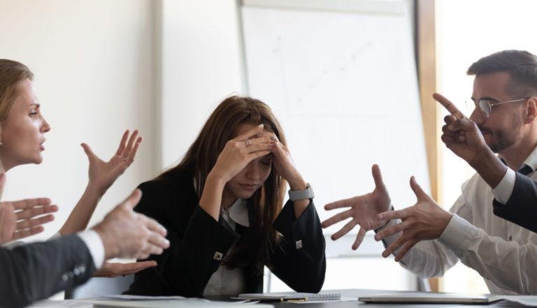 Mulher entre colegas de trabalho, num espaço de escritório, a tentar gerir conflitos no trabalho